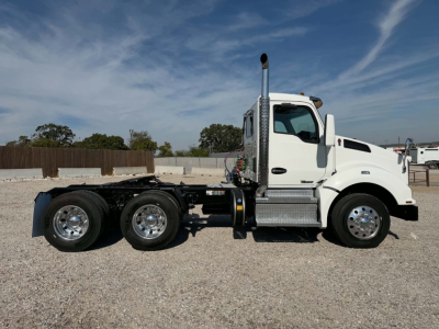 Kenworth T880 conventional daycab truck side view showing white cab, dual rear axles, chrome fuel tanks, exhaust stack, and bare chassis.