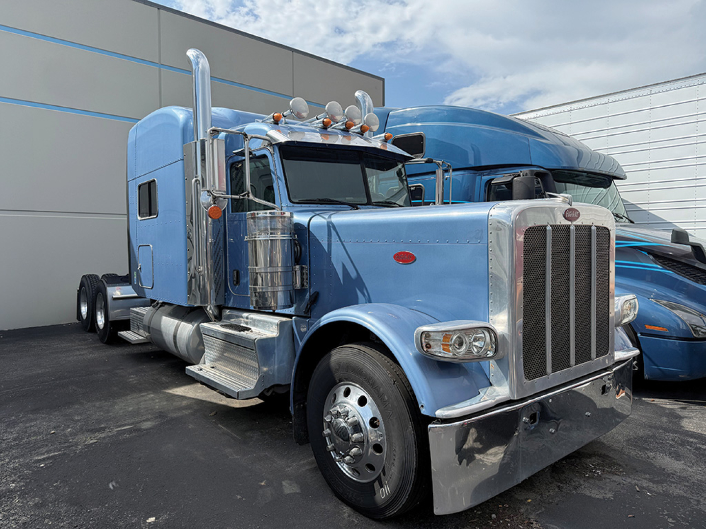 Peterbilt 389 UltraCab extended hood truck in blue side view showing chrome bumper, stack exhausts, and large grille.
