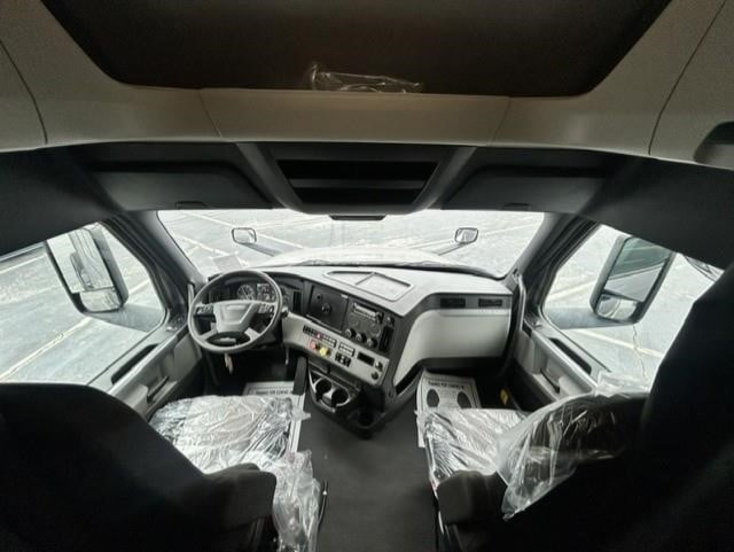 Cab interior of a 2022 Freightliner Cascadia 126 conventional sleeper truck showing steering wheel, dashboard, and plastic-wrapped seats.