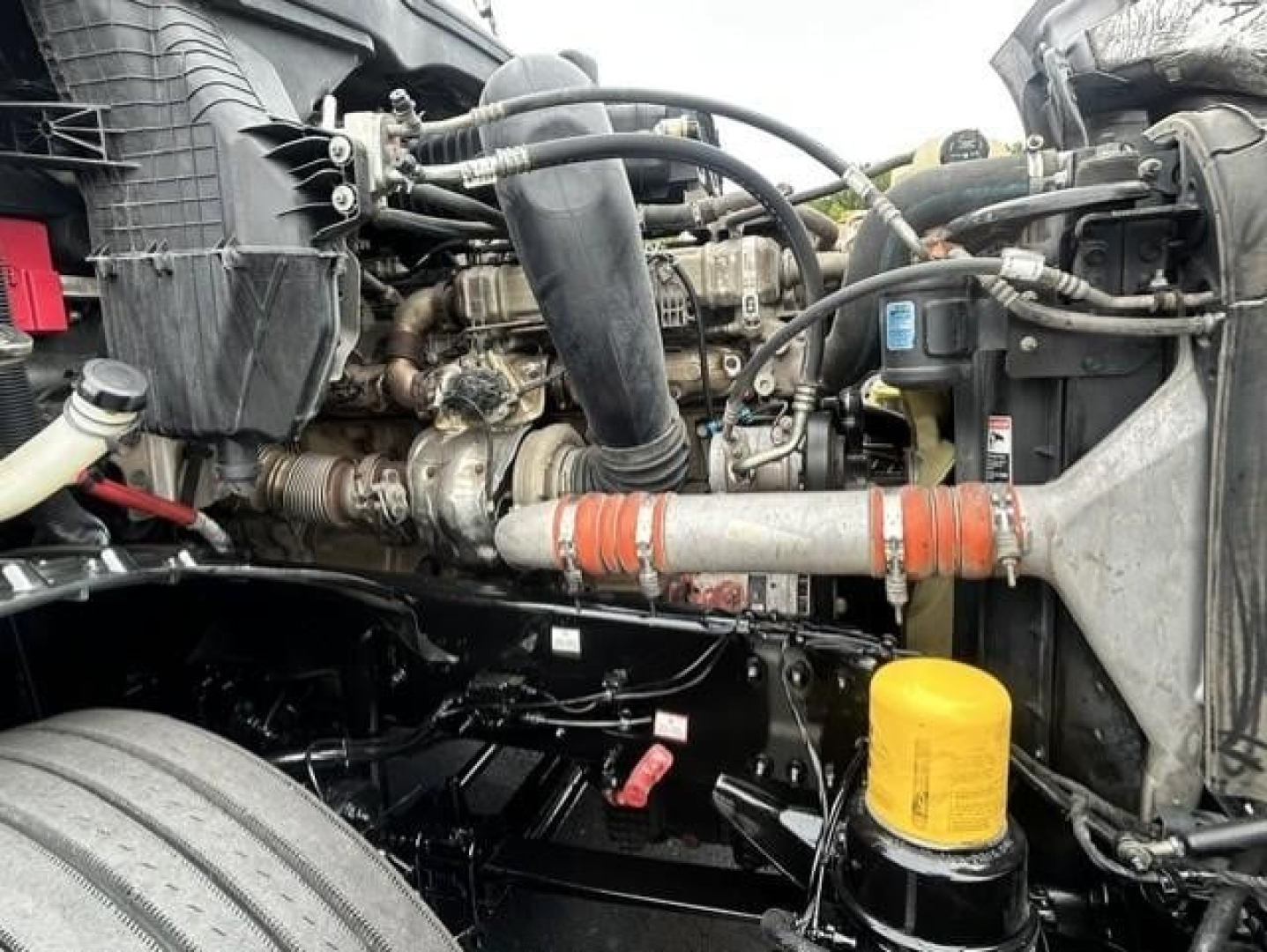 Engine bay of Freightliner Cascadia 126 showing diesel engine, coolant hoses, yellow oil/air filter canister, and surrounding components.