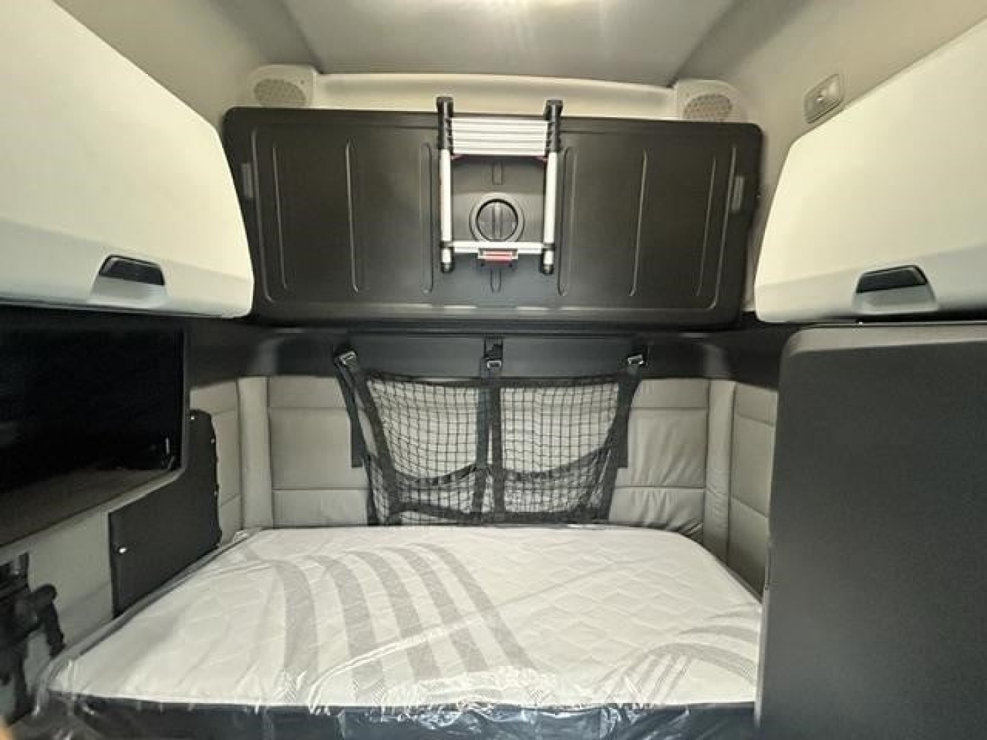 Freightliner Cascadia cab interior showing sleeper bed area with storage net and overhead cabinets.