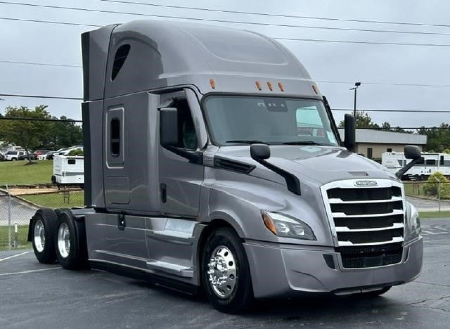 Truck cab with sleeper on a Freightliner Cascadia 126 showing front grille, headlights, large chrome bumper, dual rear axles, gray exterior, alloy wheels.