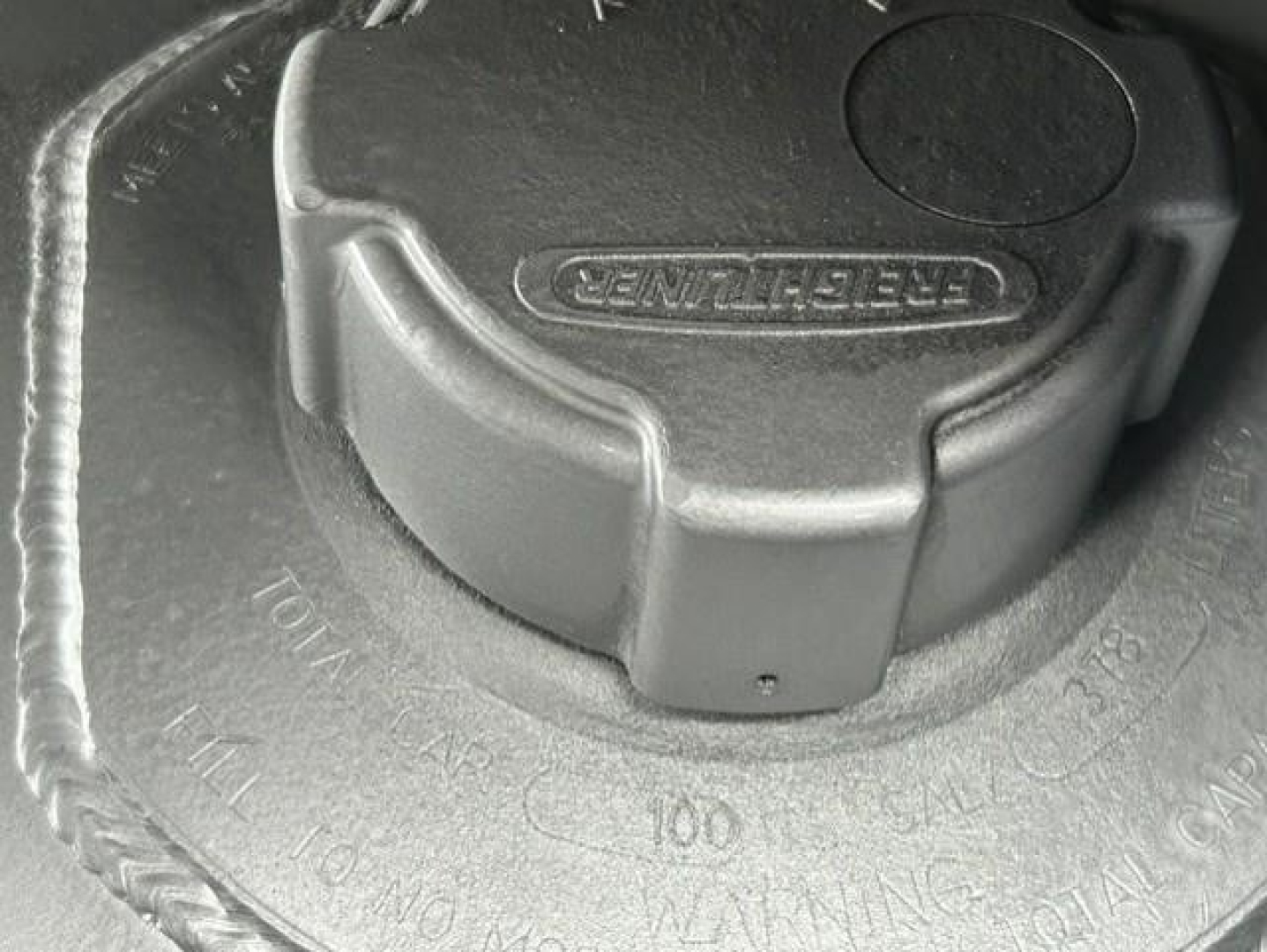 Cap with Freightliner logo on circular reservoir cap mounted in engine area, visible embossed markings around the cap.