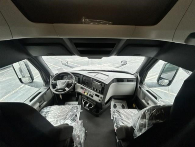 Cab interior of a 2022 Freightliner Cascadia 126 conventional sleeper truck showing steering wheel, dashboard, and plastic-wrapped seats.