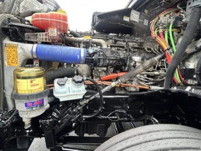 Engine bay of a 2022 Freightliner Cascadia 126 conventional sleeper showing various components: blue silicone hose, yellow oil filter, white coolant reservoir cap, red cap, wiring harness, and multiple labels.