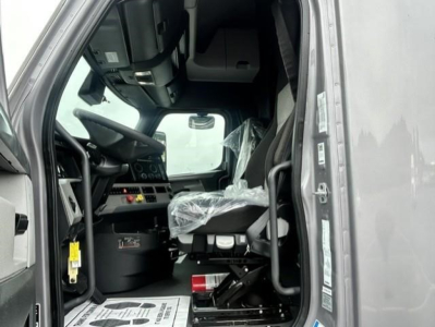 Cab interior of a 2022 Freightliner Cascadia 126 truck, front seat with plastic cover, dashboard and steering wheel visible in entry doorway.