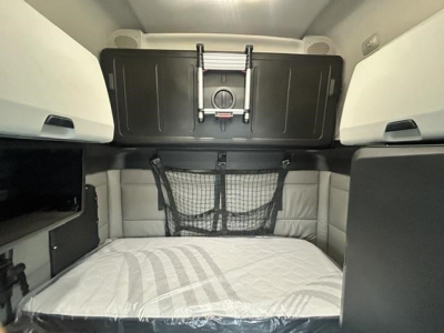 Freightliner Cascadia cab interior showing sleeper bed area with storage net and overhead cabinets.