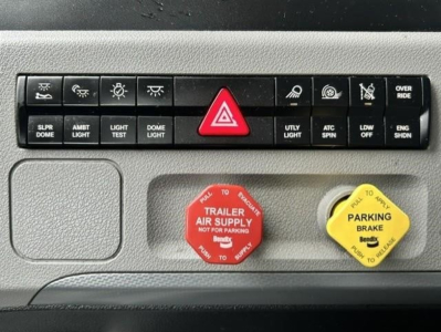 Dash panel with multiple black rocker switches and a red hazard button, red trailer air supply switch, yellow parking brake switch, and two circular red and yellow caps labeled for safety and parking brake.