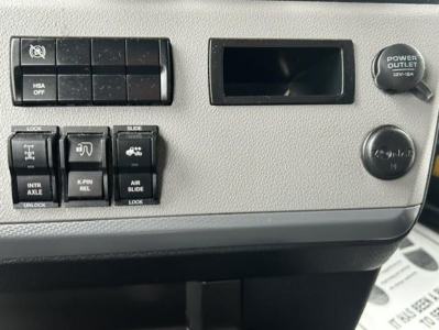 Dashboard controls of a Freightliner Cascadia showing auxiliary switches, power outlet knob, and blank display slot.