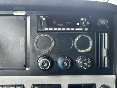 Dashboard panel of a Freightliner Cascadia showing radio unit, three circular gauges, HVAC controls, and power outlet.