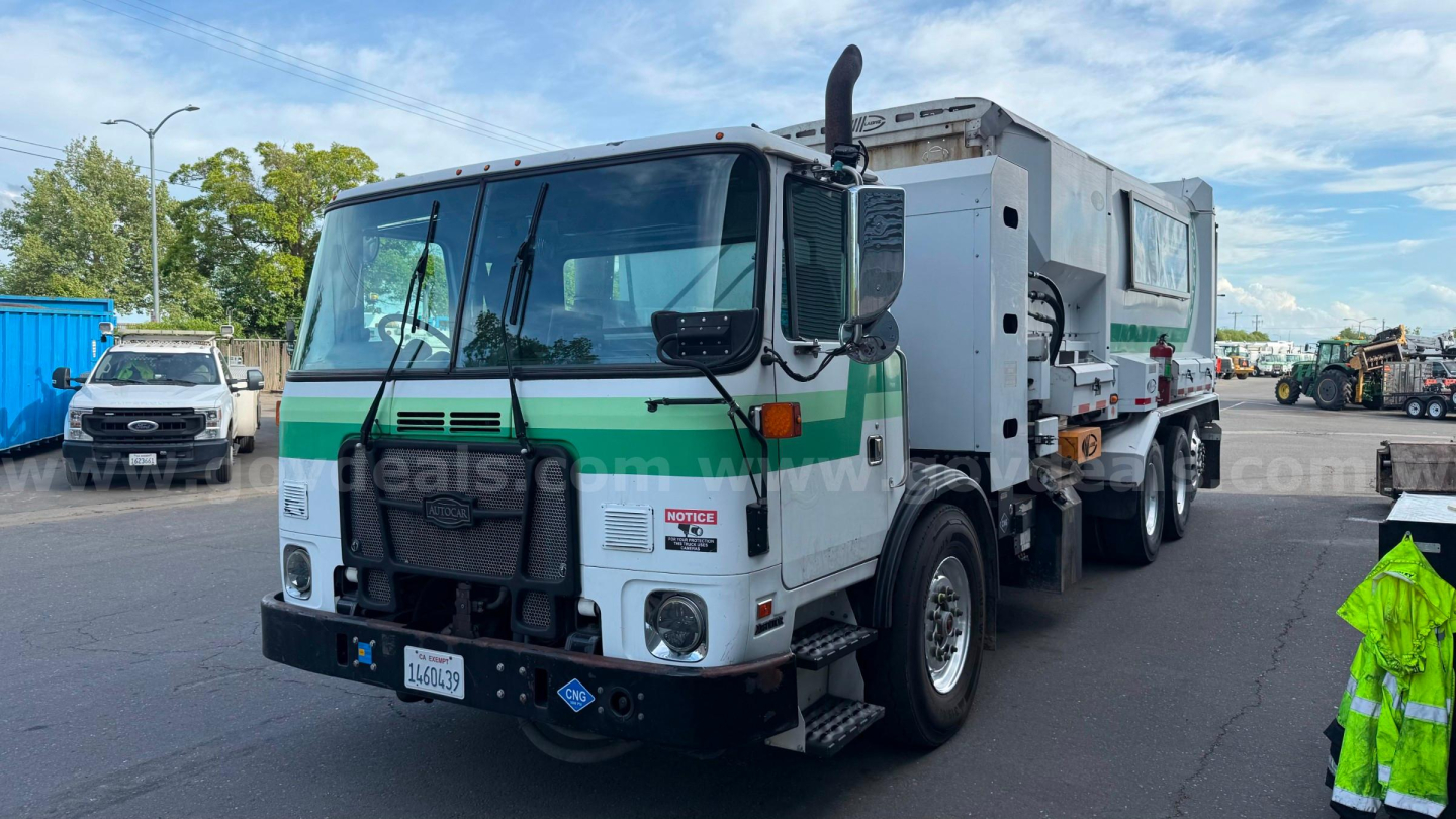 Autocar ACX XPeditor dump truck in service view showing front and side with green and white color, large cab, plow bumper, and attached hopper/compactor unit.