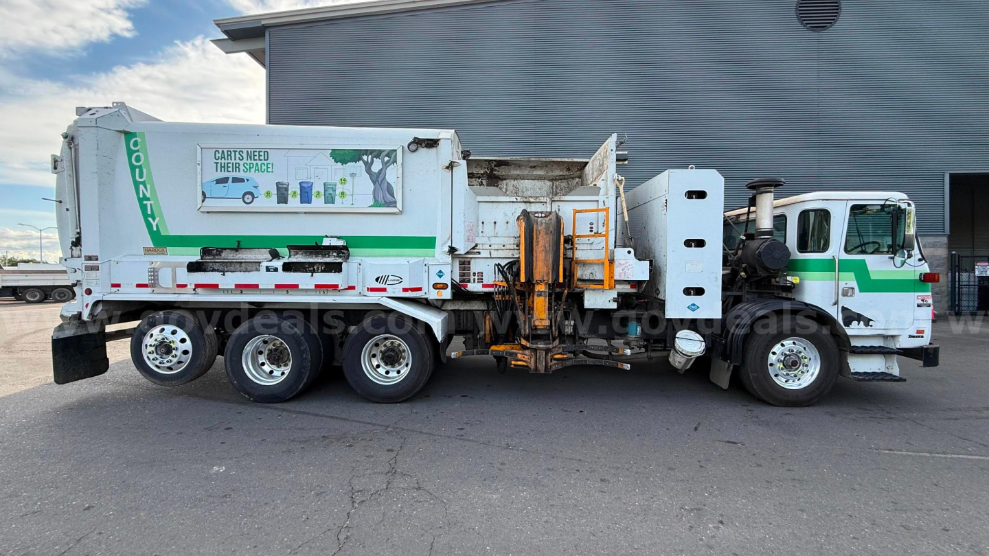 Autocar ACX Xpeditor refuse truck side view showing waste compactor and rear hopper; visible labels include COUNTY arrow and green/white cab accents.