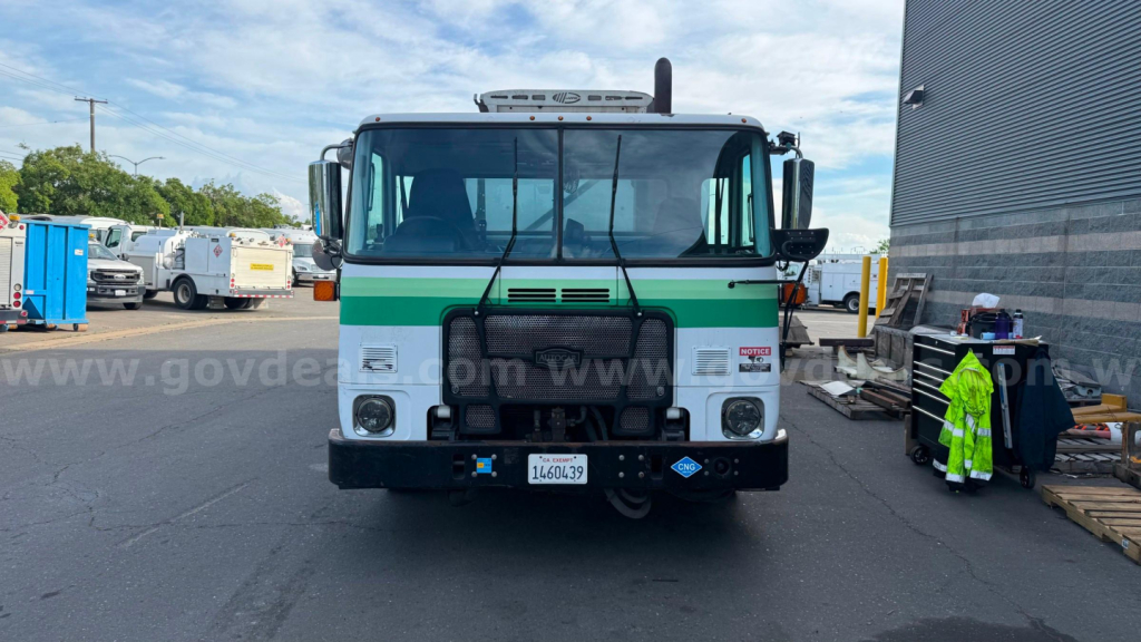 Autocar ACX XPeditor front view showing cab with green stripe, headlights, bumper, and license plate; truck in a yard.