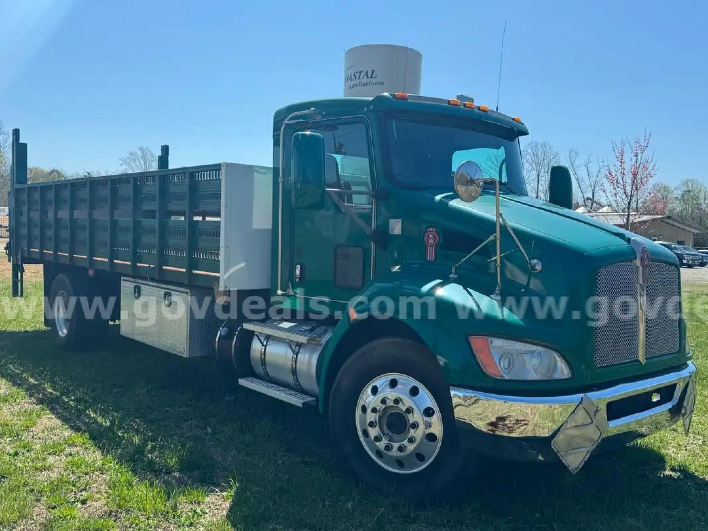Kenworth T370 flatbed truck in green, side view showing cab, long steel dump-style bed with side rails, large front bumper, and dual rear wheels.