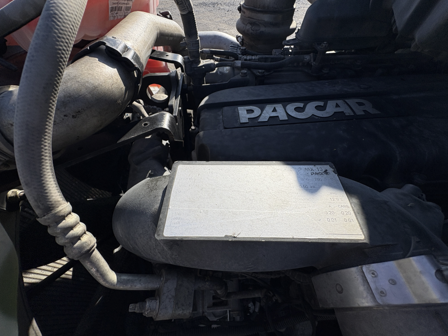 Kenworth T680 engine bay showing PACCAR cover and surrounding hoses and components.