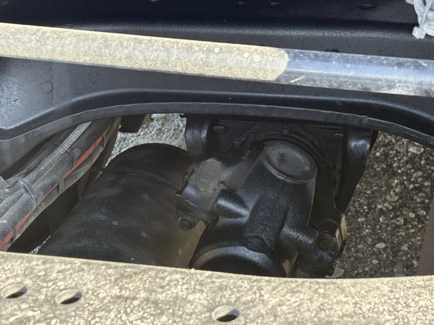 Kenworth truck component view showing a black hydraulic reservoir or air tank in a compartment with surrounding metal frame and wiring.