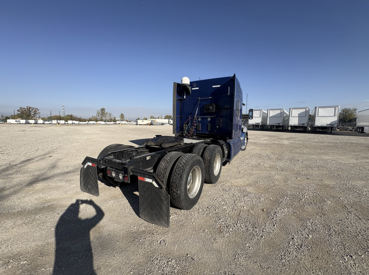 Kenworth T680 tractor trailer in blue, rear view showing dual rear axles and mud flaps.