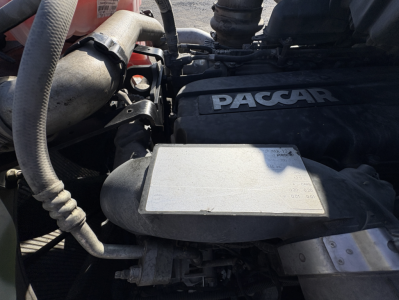 Kenworth T680 engine bay showing PACCAR cover and surrounding hoses and components.