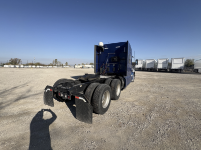 Kenworth T680 tractor trailer in blue, rear view showing dual rear axles and mud flaps.