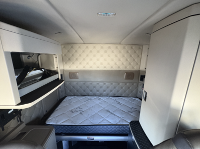 Interior of 2021 Kenworth T680 sleeper cab with quilted light gray leather panels, sleeping bed, overhead storage, and control panels visible.