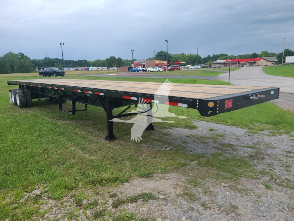 Fruehauf steel flatbed trailer with dual rear axles and wood deck, side rails, and landing legs visible in an open lot.