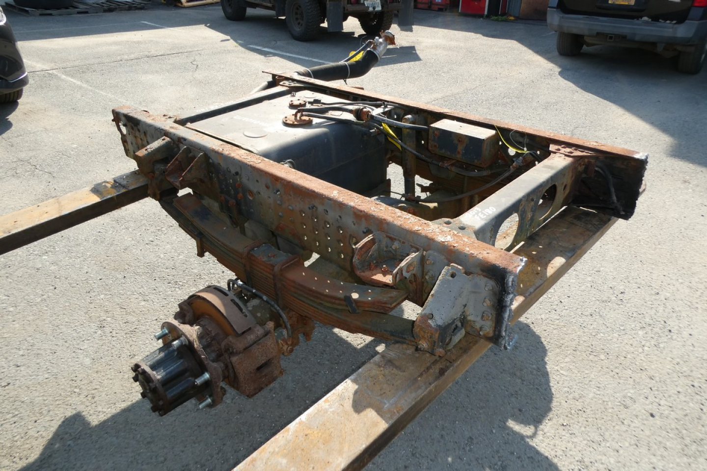 Chassis frame and front axle assembly of a Mitsubishi Fuso FE180 cab and chassis. Rusty frame with exposed suspension components and driveline area.