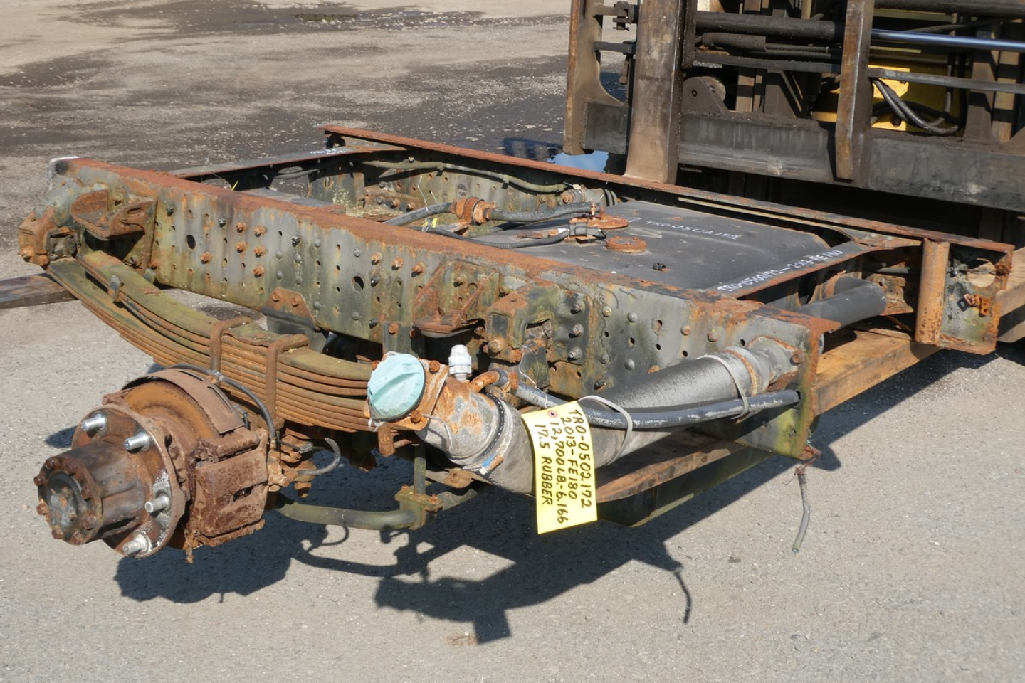 Chassis frame with rear axle and wheel hub, fuel tank, and exhaust attached; tag on hose and bolts visible.