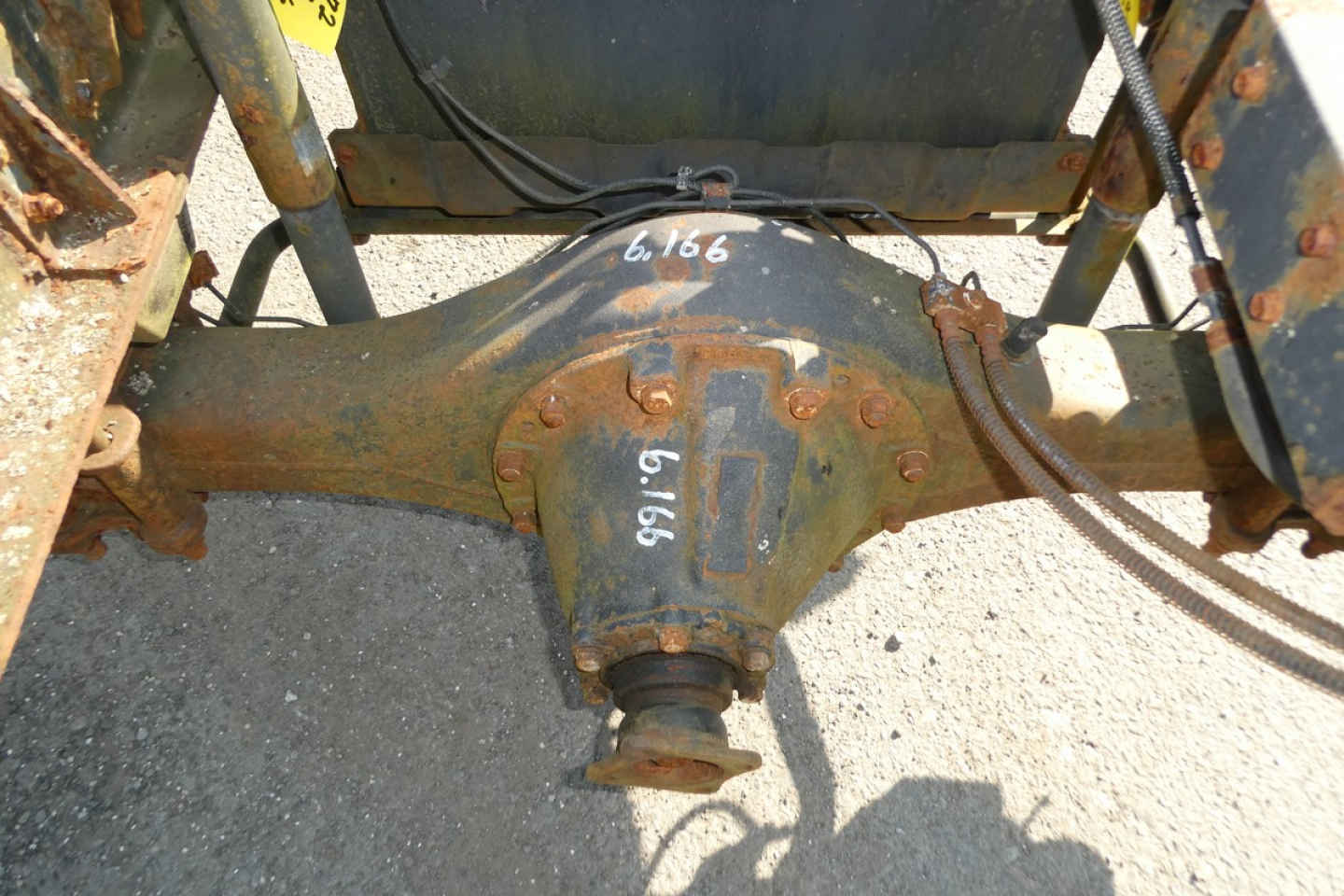 Rear view of a rusty truck differential/axle housing with tag numbers 6166 and 1917 handwritten; part of a rusty drivetrain on a Mitsubishi Fuso FE180 chassis.