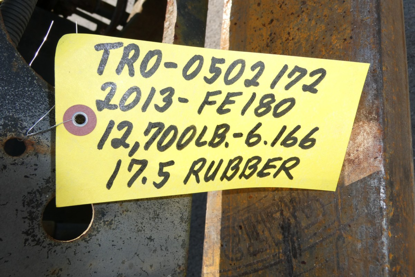 Yellow tag with handwritten black text: 'TR0-0502 172 2013-FE180 12,700LB-6.166 17.5 RUBBER' attached to metal surface.