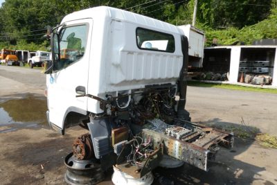 Cab and chassis showing exposed engine bay area on a white 2013 Mitsubishi Fuso FE180 front-left view with removed front body panels.