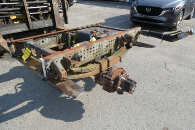 Chassis frame and partial suspension components of a Mitsubishi Fuso FE180 cab and chassis showing rusted frame rails, leaf springs, and hub with wheel studs.