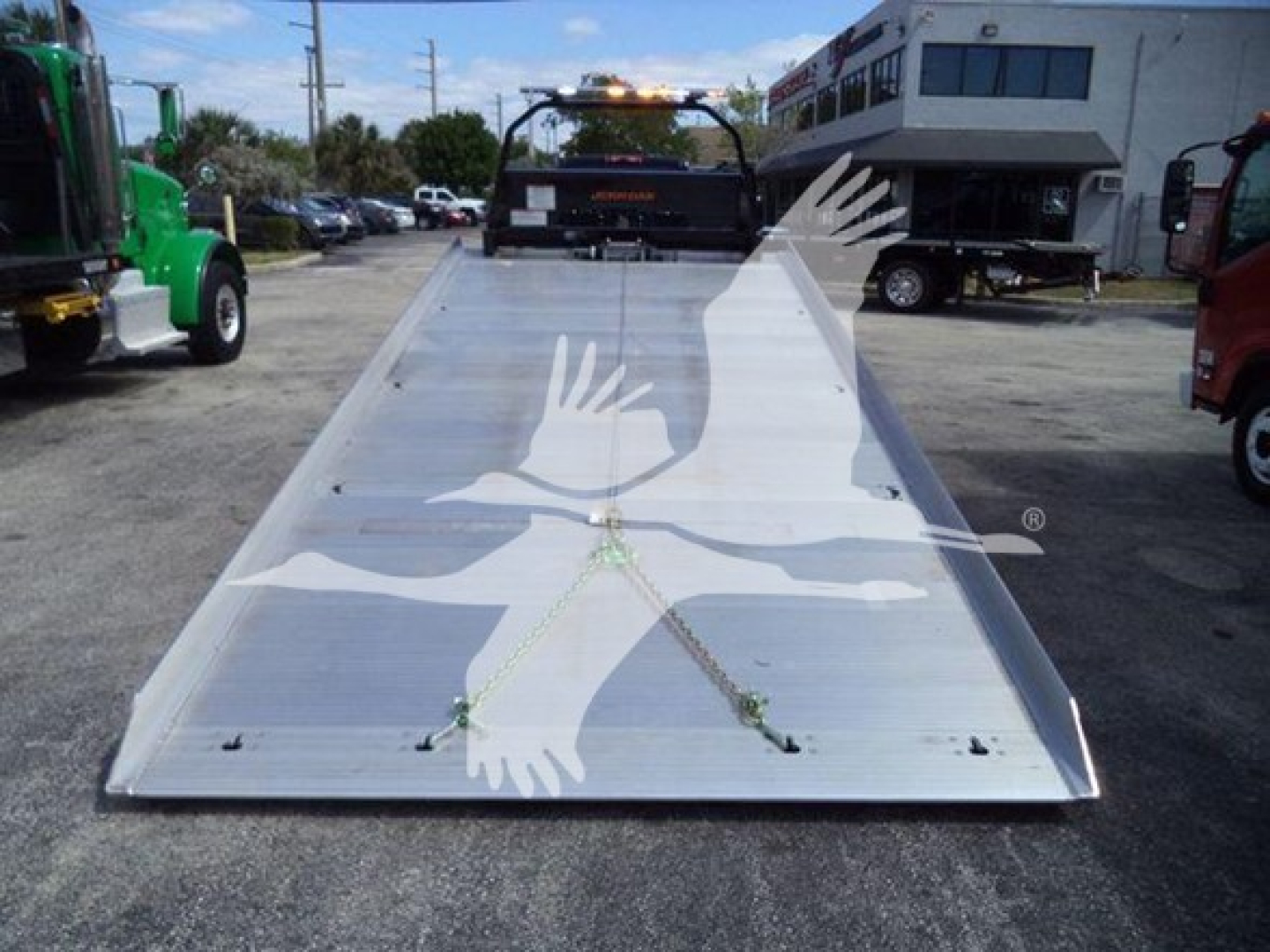 Roll-back truck bed with aluminum surface, two green stanchions, and a white crane logo overlay in the foreground.