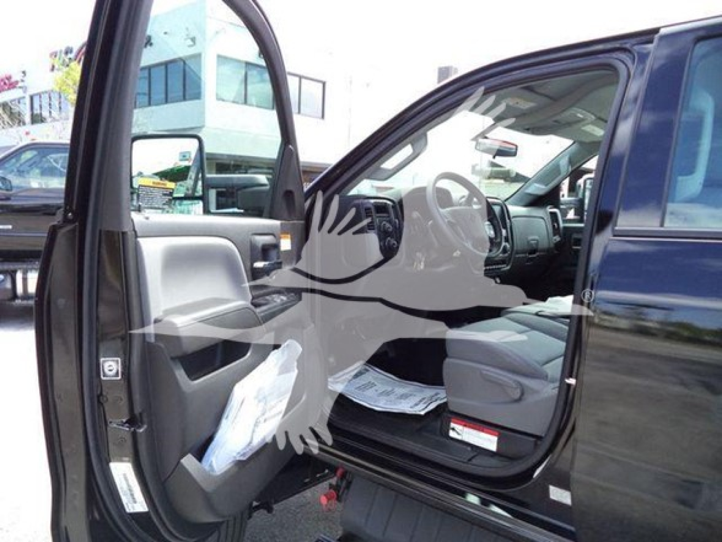 Truck cab interior view with open driver door showing steering wheel and dashboard; documents on seat; exterior of blue truck visible.
