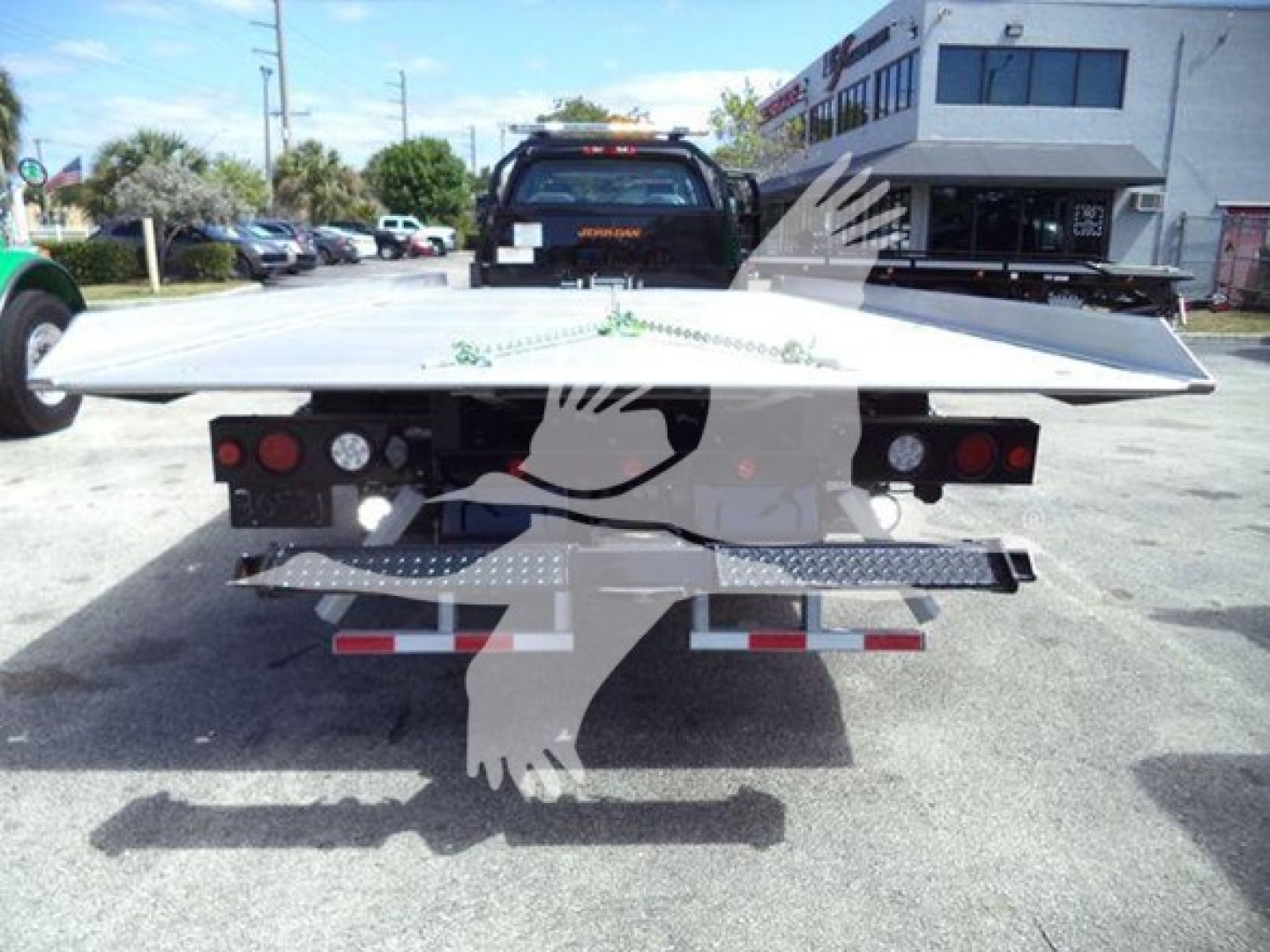 Flatbed tow truck rear view with metallic platform and red taillights in a dealership lot.