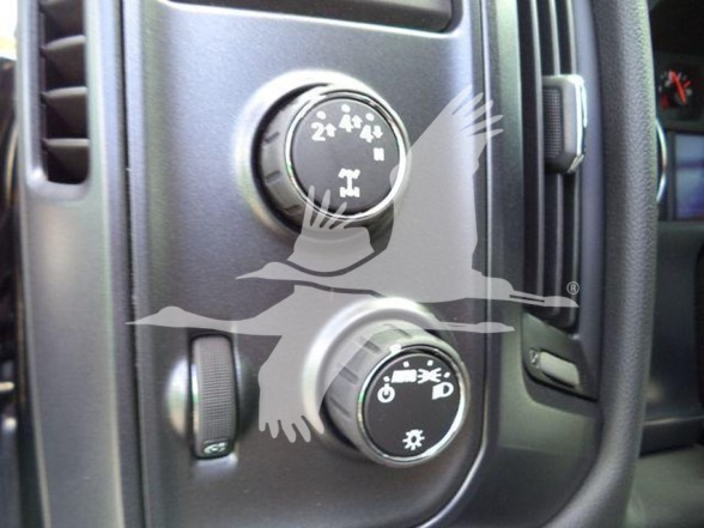 Panel with two round knobs in a vehicle dashboard, one showing four-wheel drive icons and the other climate control symbols.