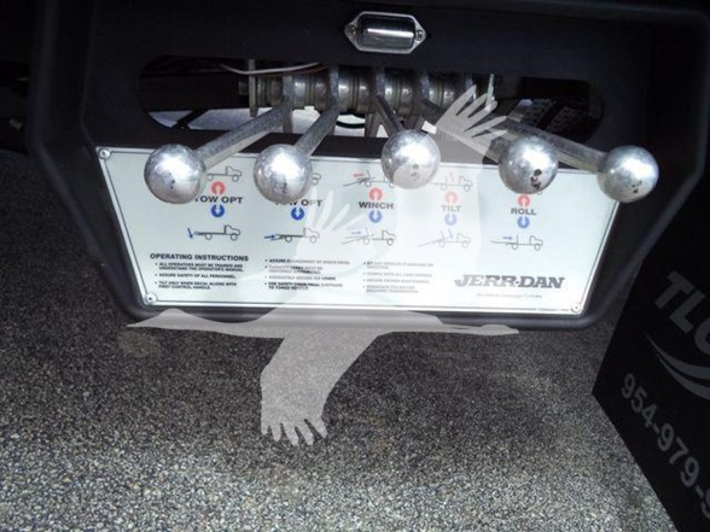 Truck control panel with multiple metal levers and wiring, showing labels and diagrams for operating the rollback winch and jug features on a Jerr-Dan system.