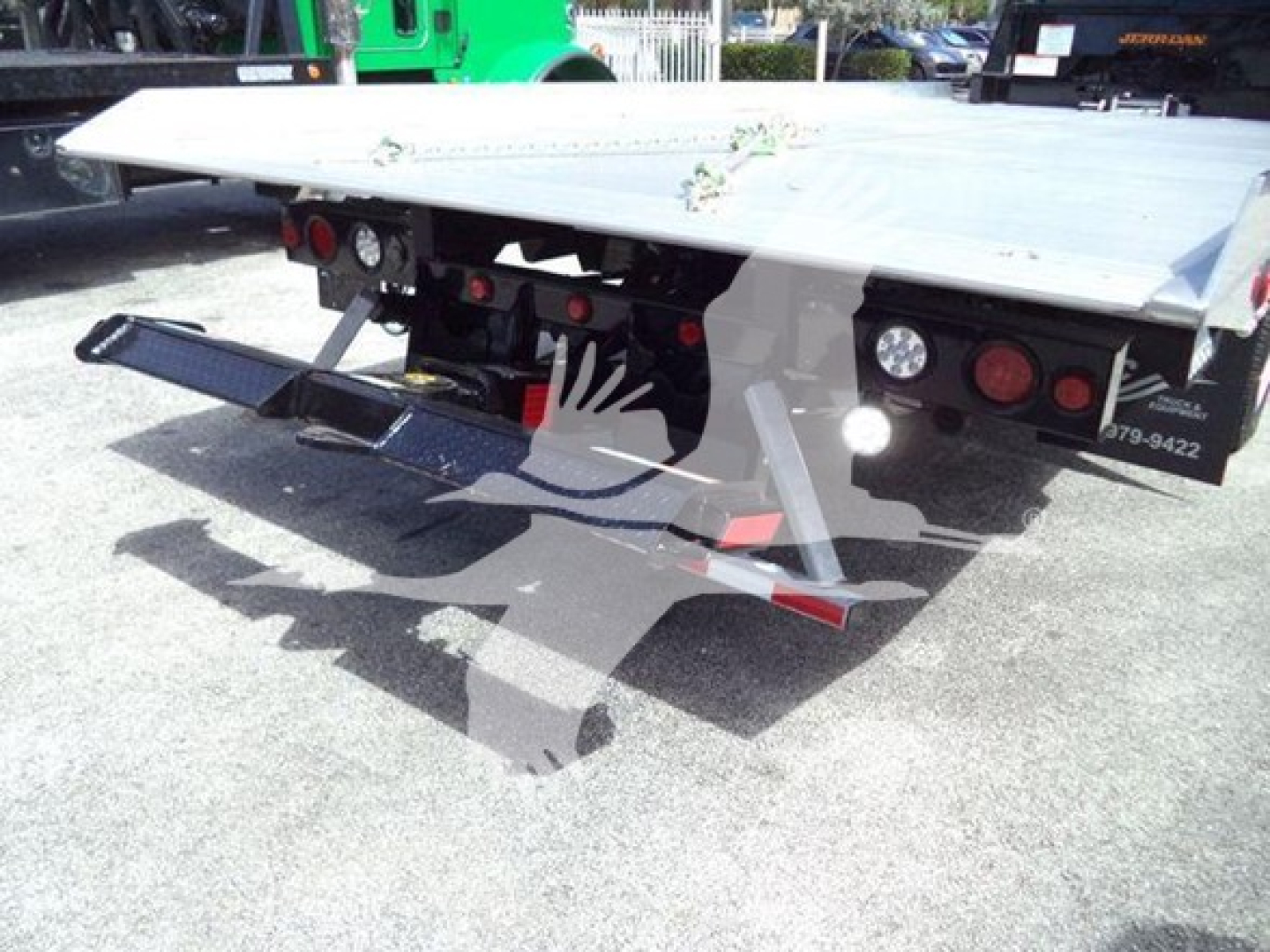 Truck bed of a 2023 International CV rollback tow truck showing flatbed and rear bumper lights with hydraulic components.