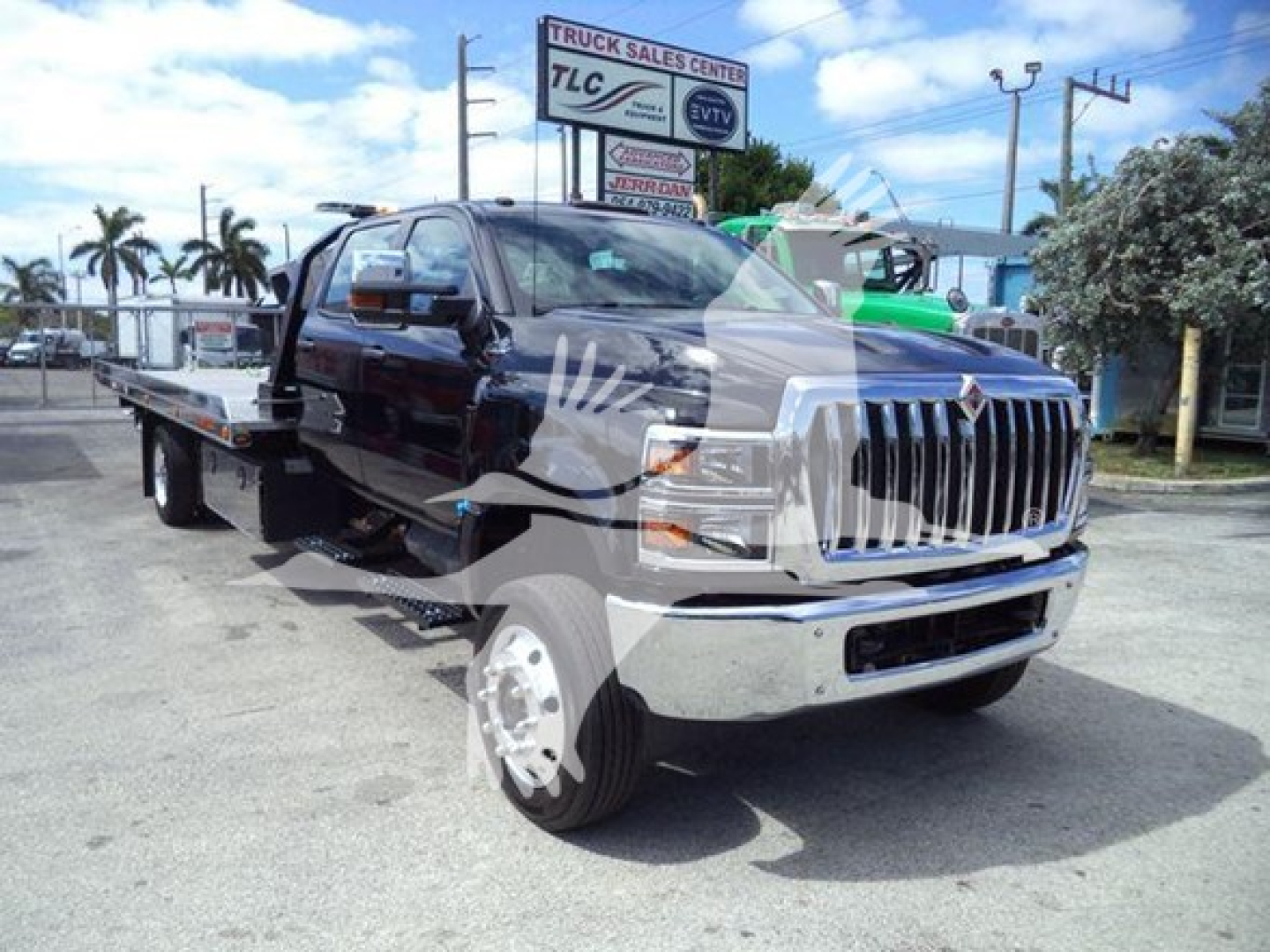 Tow truck/rollback truck with chrome grille and flatbed, International logo on grille, license plate area front; dealership sign in background.