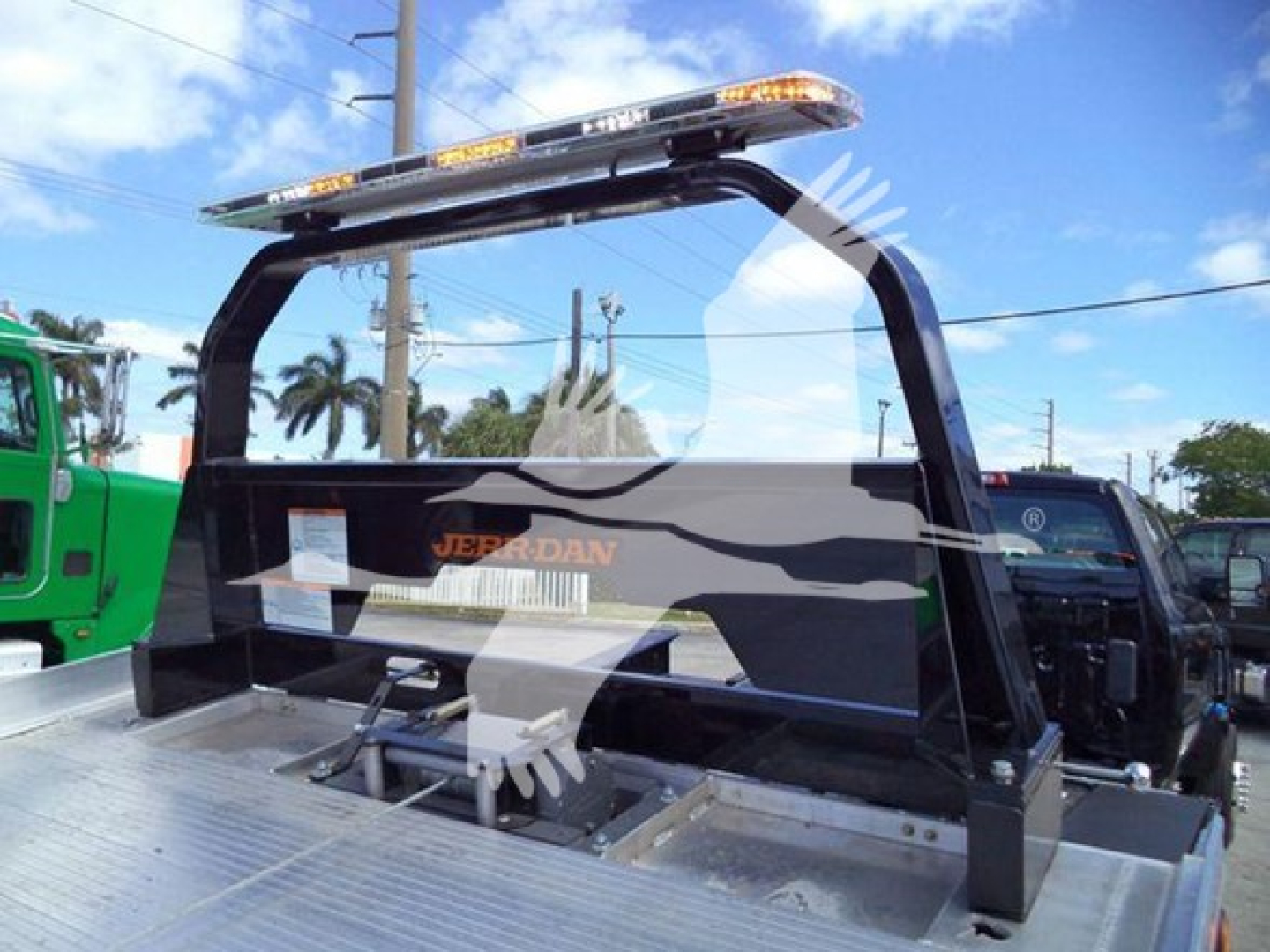 Truck bed with rollover frame and light bar showing Jeps... branding and a winch mechanism; cab and rear platform visible in background.