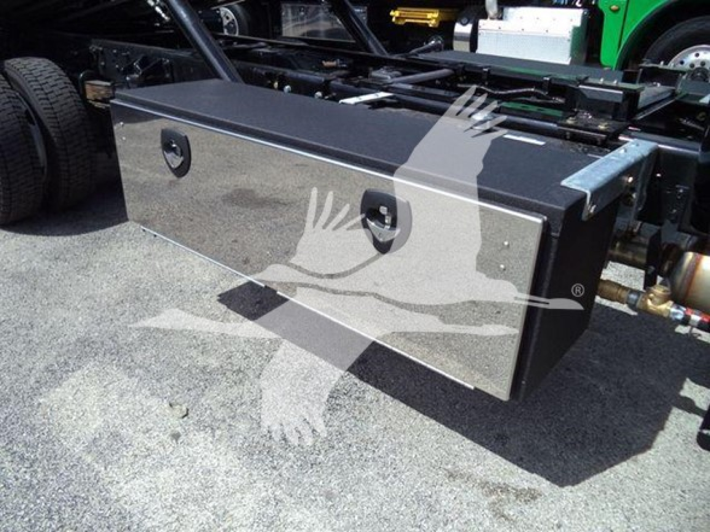Toolbox/box mounted on truck chassis with two circular latches, metallic finish, undercarriage visible.