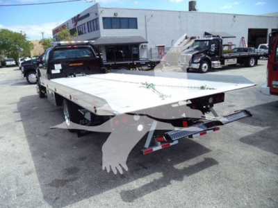 Tractor-trailer tow truck showing a flatbed with dovetail and rear lights; International CV Series truck in a lot with other vehicles.