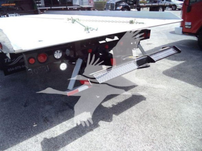 Truck bed with hydraulic rollback equipment and steps; visible lights and metal frame under trailer.