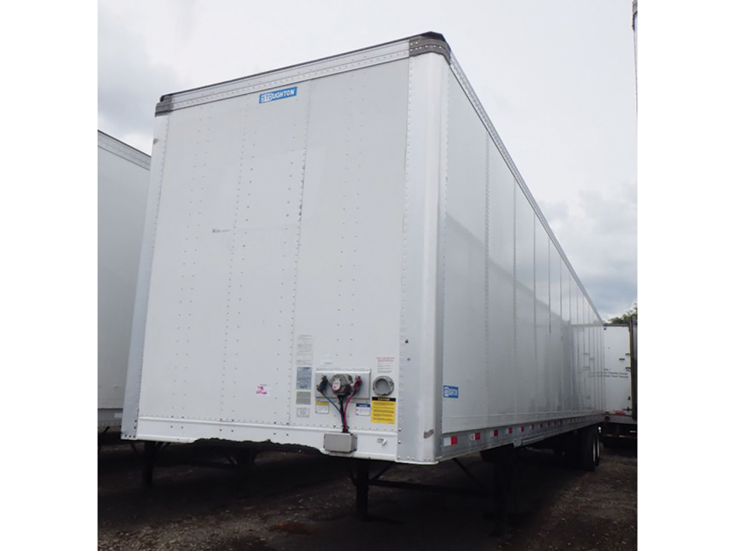 Trailer side and rear showing a white Stoughton plate van trailer with reflectors and labeling on the corners and a hitch area visible.