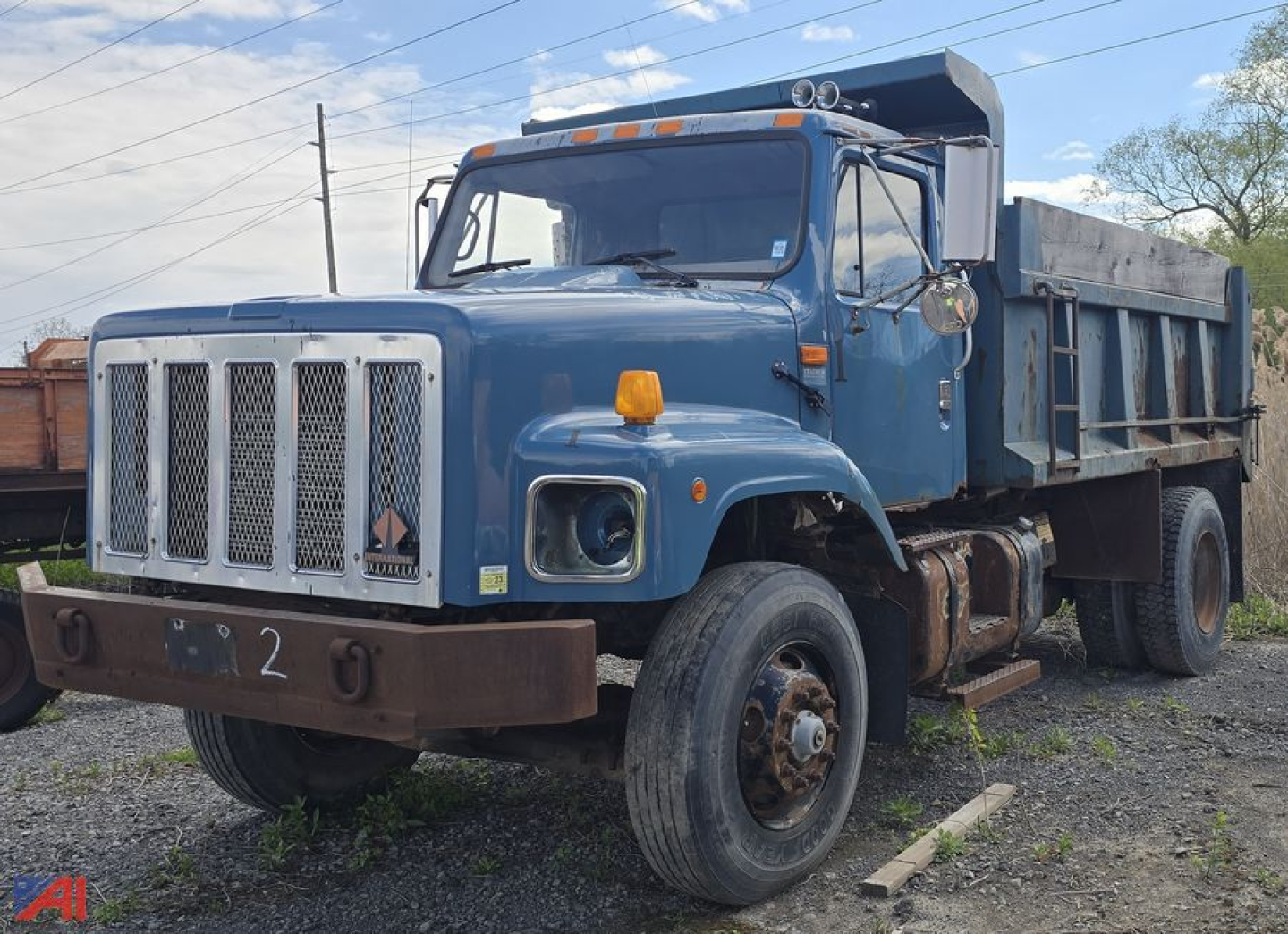 Open-cab blue 2002 International 2674 dump truck with large front grille, single cab, and dump bed; shows front left wheel, bumper, and orange marker light.