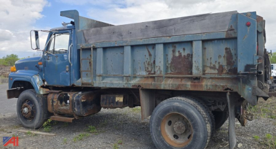 Dump truck side view showing blue cab and rusted dump bed with large rear tires and worn body.