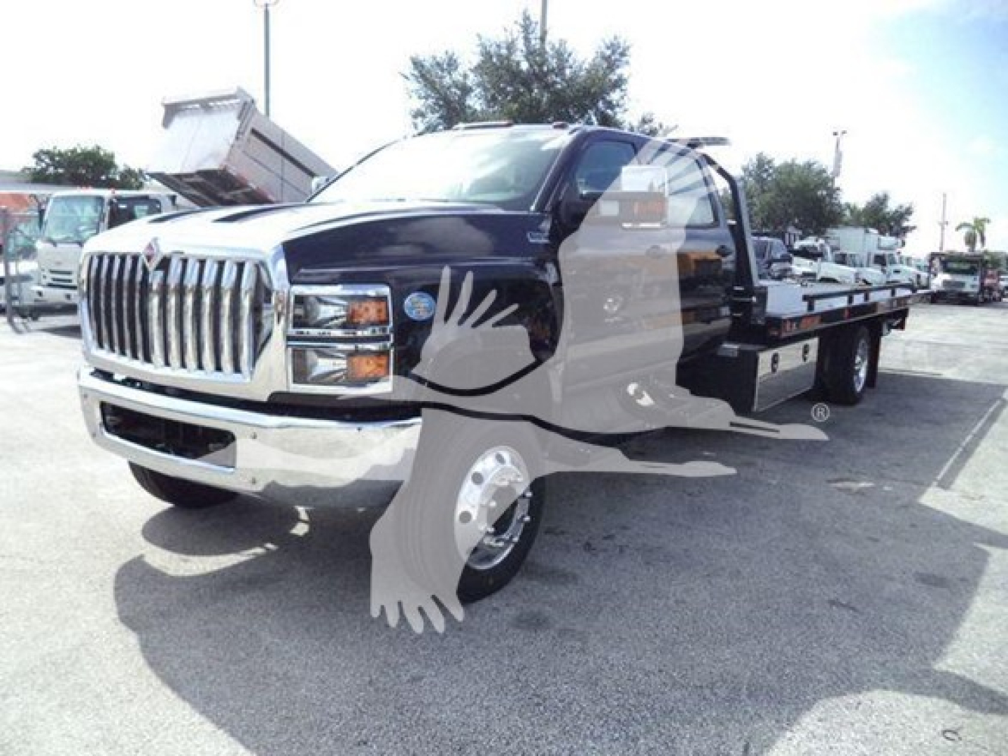 International CV Series truck in a dealership lot showing a black crew cab and flatbed rollback equipment under bright daylight.