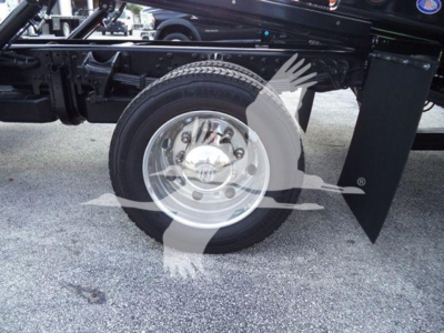 Truck wheel and fender area with circular logo watermark overlay. Visible are wheel, hub, tire, and chassis components.