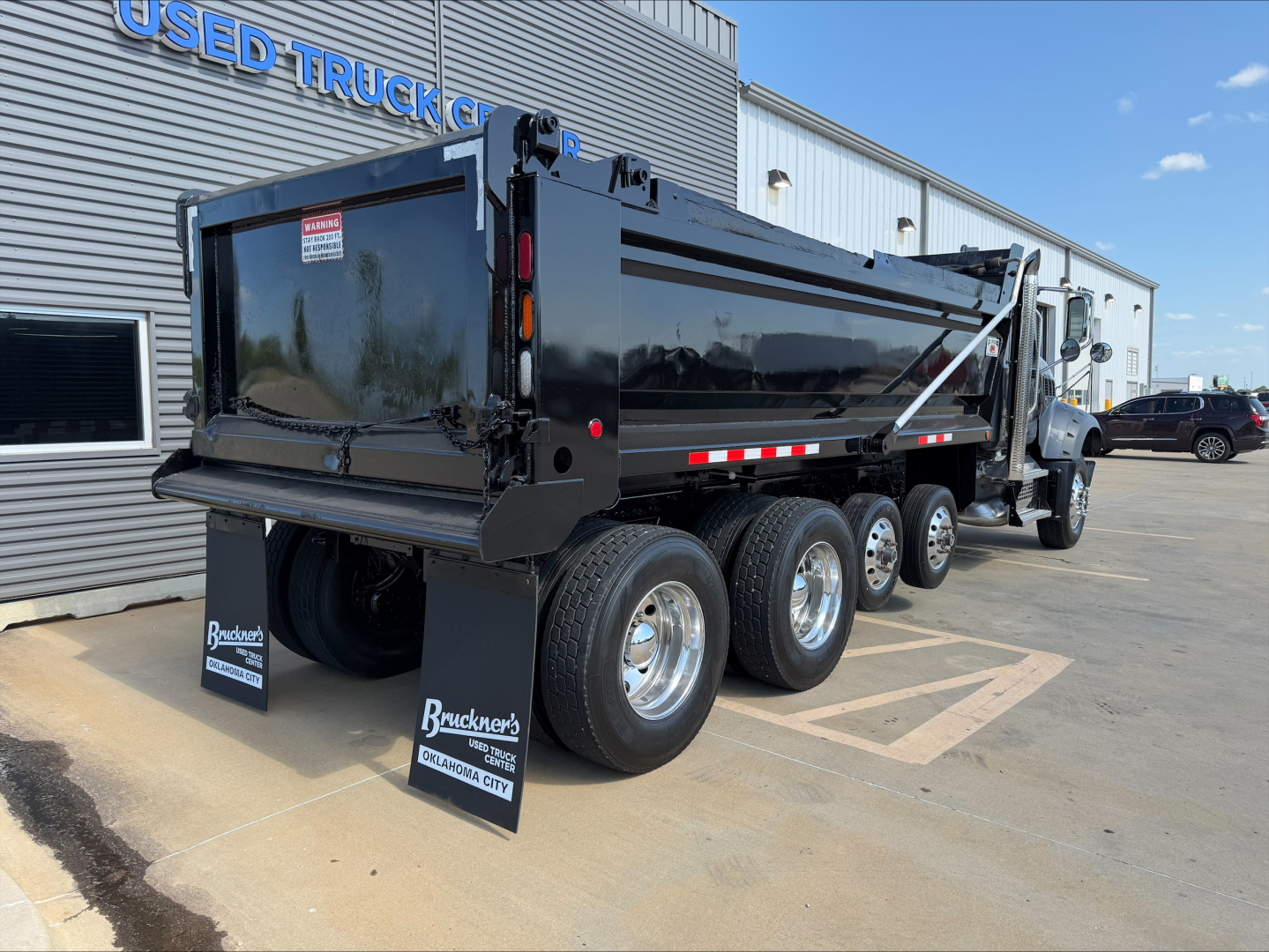2023 Mack GR64F dump truck rear and side view showing black dump box, triple rear axles, and rear mudflaps with branding.