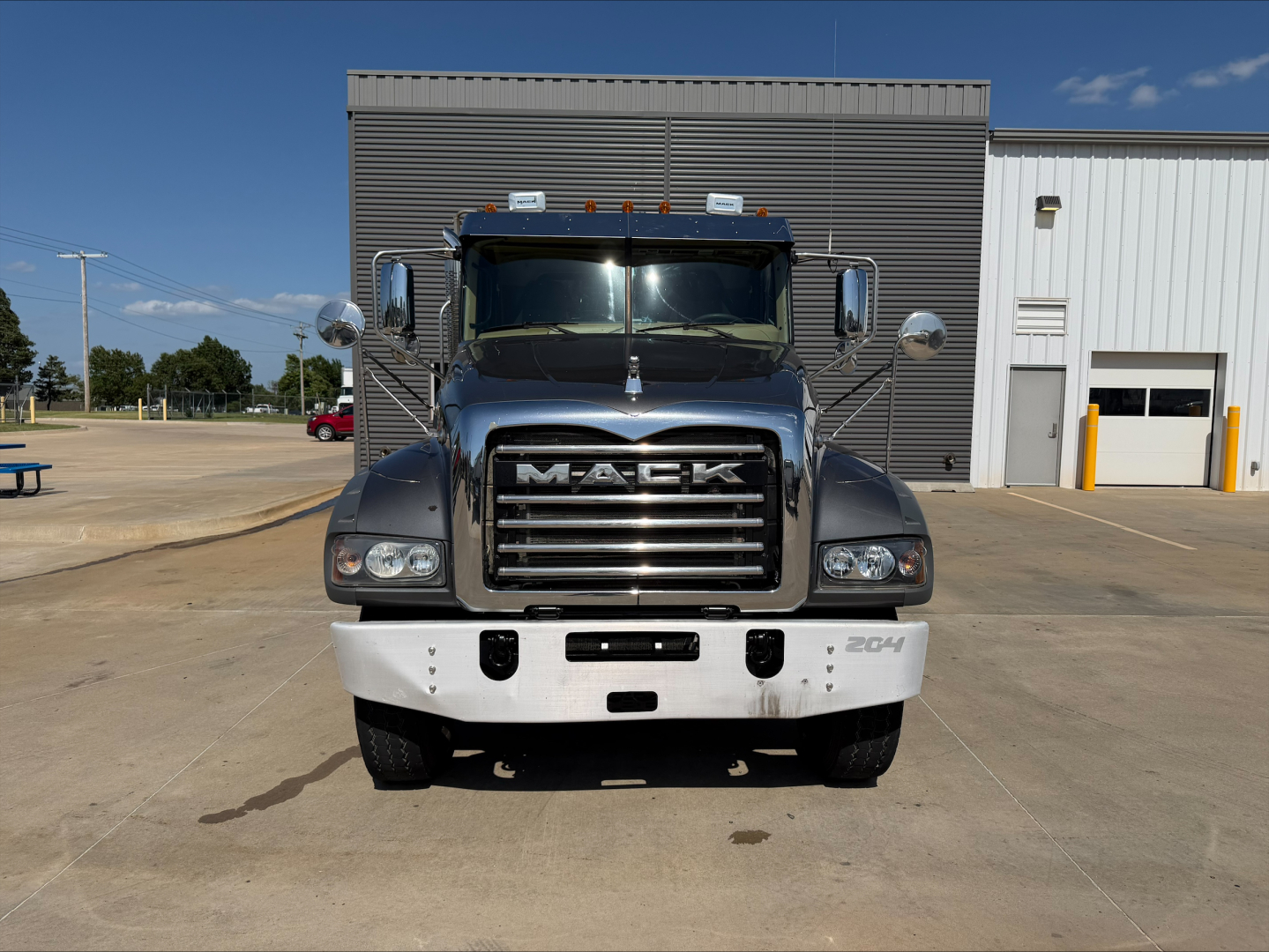 Mack GR64F dump truck front view showing chrome grille with MACK lettering and bumper, 2644 badge on right side, daytime, industrial building in background.