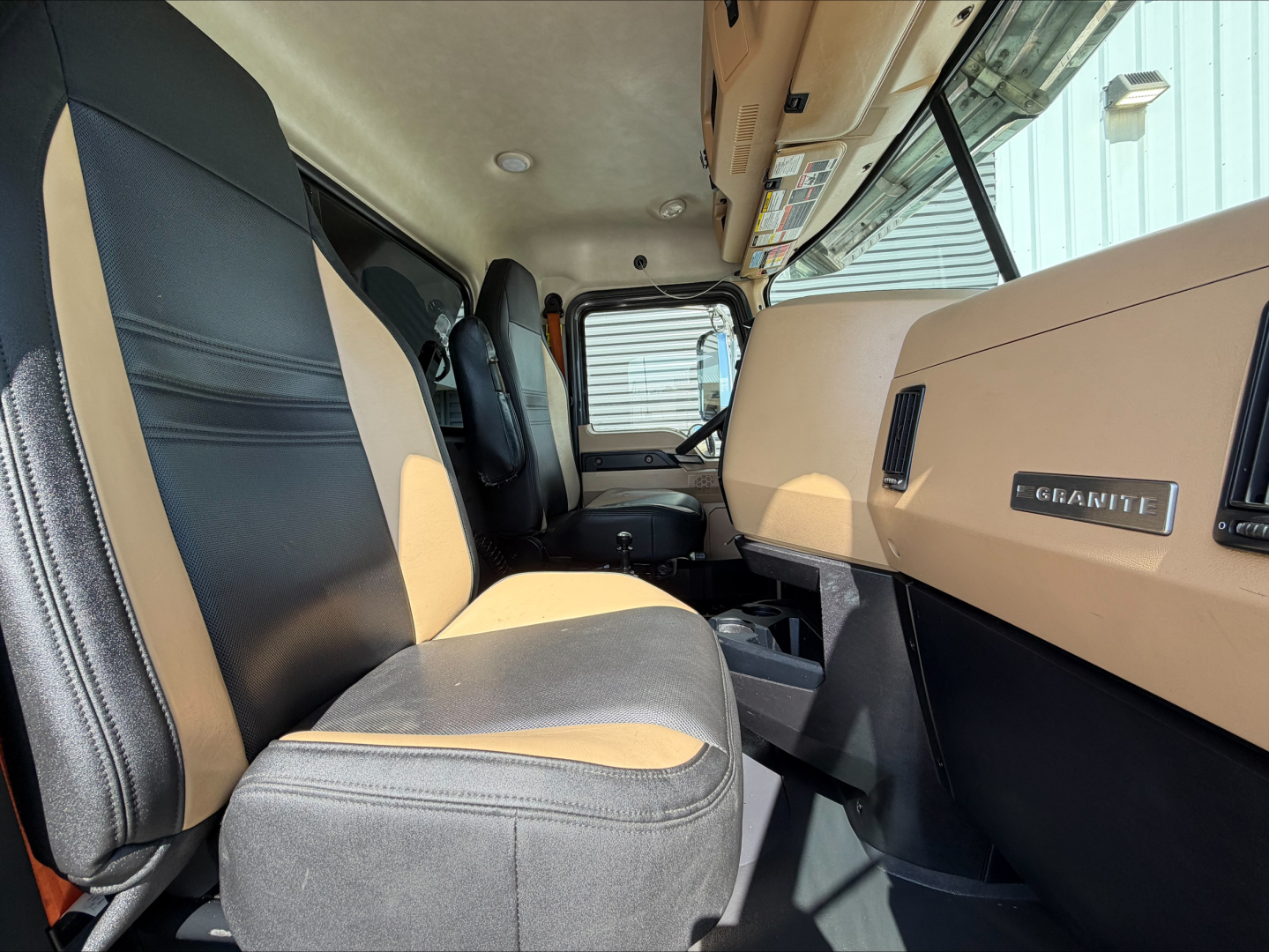Interior of 2023 Mack GR64F truck cab showing beige and black seats, dashboard with 'GEHANTe' badge? and steering area.